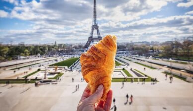 ヨーロッパの食べ物として絶大な人気を誇るフランス本場のクロワッサン。パリの象徴であるエッフェル塔を背景に、サクサクに焼き上がった大きなクロワッサンを手に掲げている風景