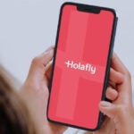 海外旅行でのHolafly eSIMの利用イメージ。Holaflyのロゴが表示されたスマホを持つ人