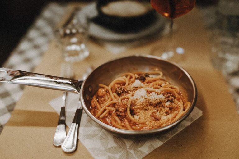 ヨーロッパの人気グルメであるイタリアの定番パスタ「アマトリチャーナ」。トマトと豚肉のソースが絡んだ太めの麺にたっぷりの粉チーズがトッピングされ、フライパン型の器のままテーブルに提供されているレストランでの様子