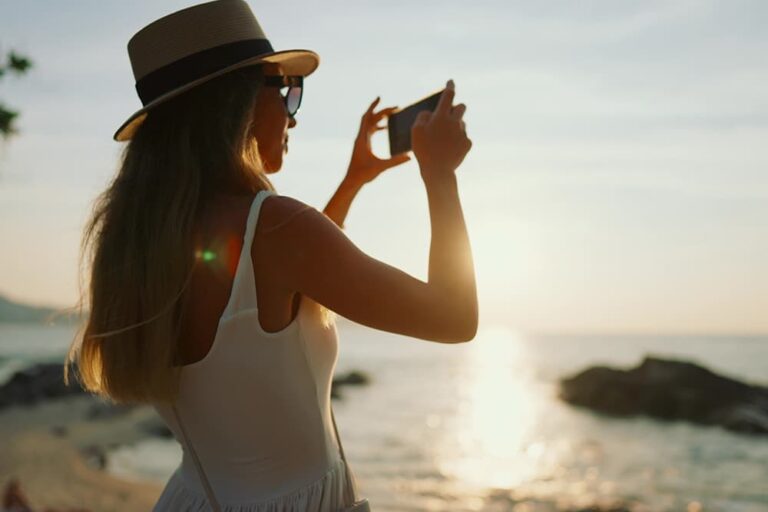 海外旅行先のリゾート地の海岸で、20ギガのデータ通信を活用しながらスマートフォンで景色を撮影する旅行者の様子