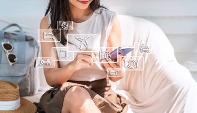 スマホを操作する女性の周囲に、タクシーや飛行機などの旅行アイコンが重ねられたイメージ