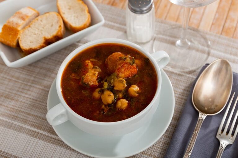 スペインの伝統的な食べ物「コシード」。ひよこ豆や肉がたっぷり入った煮込みスープとパンがテーブルに並んでいる様子