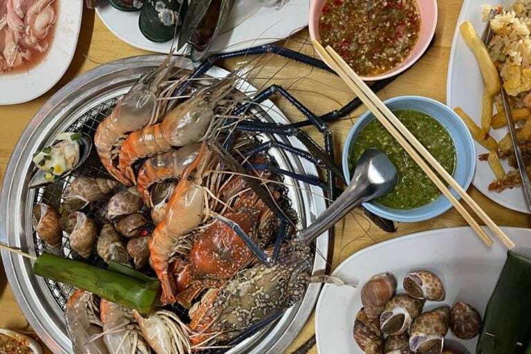 プーケットやクラビなどでも人気を集めるタイの新鮮な食べ物「シーフードのグリル」。網の上で豪快に焼かれる大きなエビやカニ、貝類と、スパイシーなつけダレが並ぶテーブルの様子