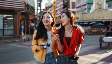カメラとスマートフォンを手に、街中で英会話を楽しむ2人の旅行者