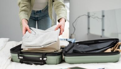 旅行の持ち物として衣類を開いたスーツケースに詰める女性の様子