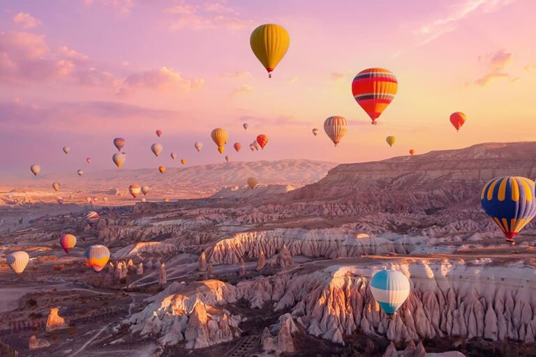 朝焼けのピンク色の空に無数の熱気球が浮かぶ、おとぎ話のようなトルコ・カッパドキアの奇岩群の風景