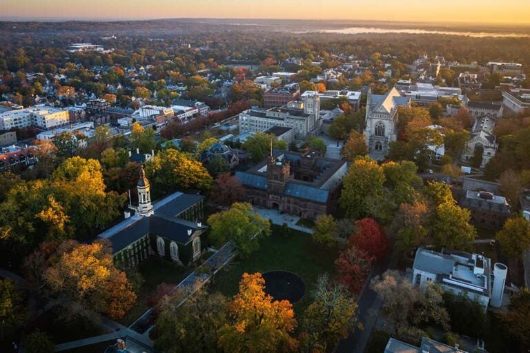 夕日に照らされるプリンストン大学の歴史的建造物群と紅葉した樹木が広がるキャンパスの空撮景観