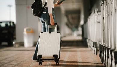 空港で白いスーツケースを引いて歩く旅行者の後ろ姿。マイナンバーカード等の必需品を準備し、海外旅行へ出発する様子。