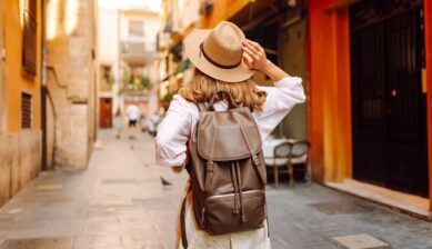 秋の温かい光が差し込むヨーロッパの街並みを、帽子とリュック姿で爽やかに散策する女性の後ろ姿