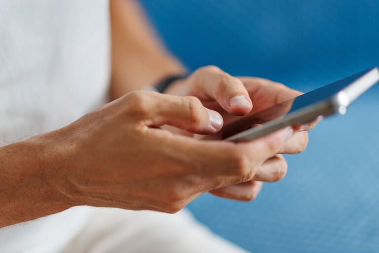 スマートフォンを手にして操作する男性の手元。旅先で海外旅行保険の緊急連絡先やサポート窓口へ問い合わせる様子を表したイメージ