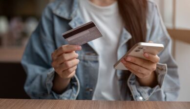 クレジットカードとスマートフォンを両手で持つ女性の姿。記事全体の主題である「海外旅行保険は入るべきか・クレジットカード付帯保険の確認事項と選び方」を表したアイキャッチ（サムネイル）イメージ。