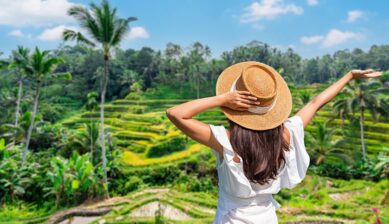 青空のもと豊かな緑が広がるバリ島のライステラス（棚田）を見渡しながら、両手を広げて開放感を味わう麦わら帽子の女性。初めての海外旅行におすすめの国や地域の選び方と準備を解説する記事のアイキャッチ画像