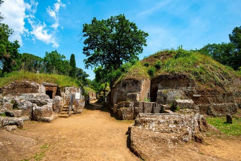 青空の下、緑に覆われたエトルリア時代の円形墳墓（ネクロポリ）が点在するチェルヴェーテリの古代遺跡