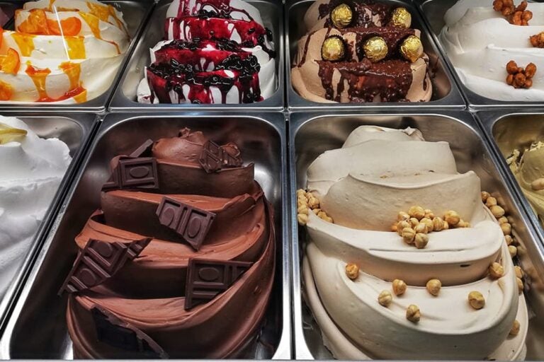 ショーケースのトレイにチョコレートやヘーゼルナッツなどの様々なフレーバーが美しく盛られた、イタリア全土で広く愛される定番スイーツ「ジェラート」