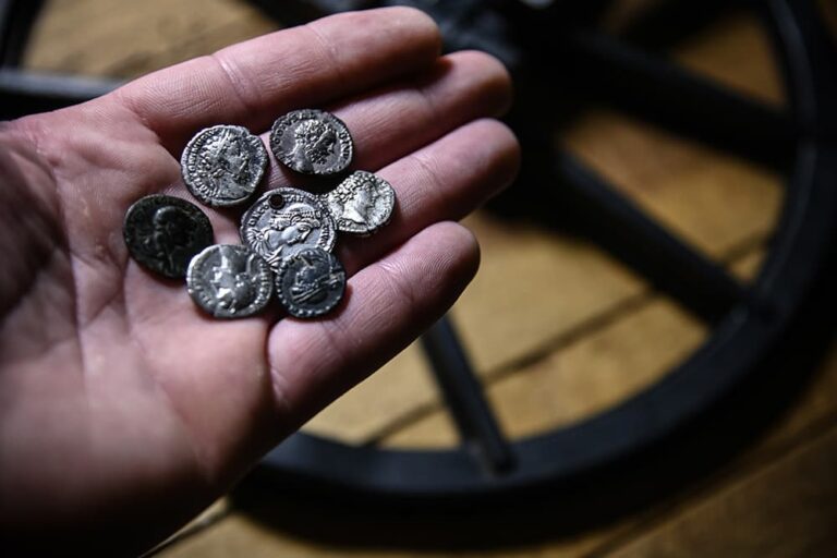 ローマのお土産として人気の、古代ローマの硬貨をモチーフにしたアンティーク調のコイン型アクセサリーを手のひらに乗せている様子