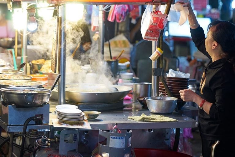 台北の「饒河街観光夜市」で湯気を上げる活気ある屋台。地元グルメを手際よく調理する店員の姿から、台湾夜市のローカルな熱気が伝わる一枚