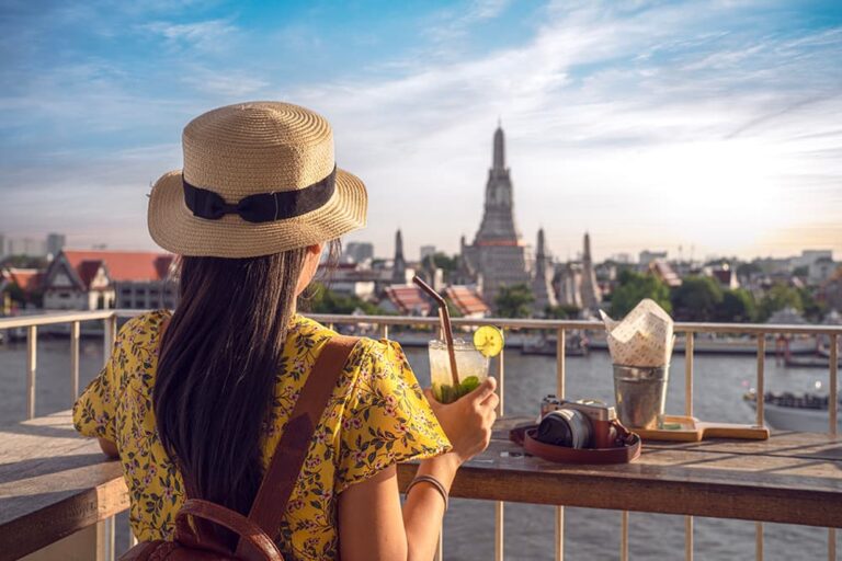 乾季の澄んだ空のもとリバーサイドカフェからワット・アルン（暁の寺）を眺める女性観光客
