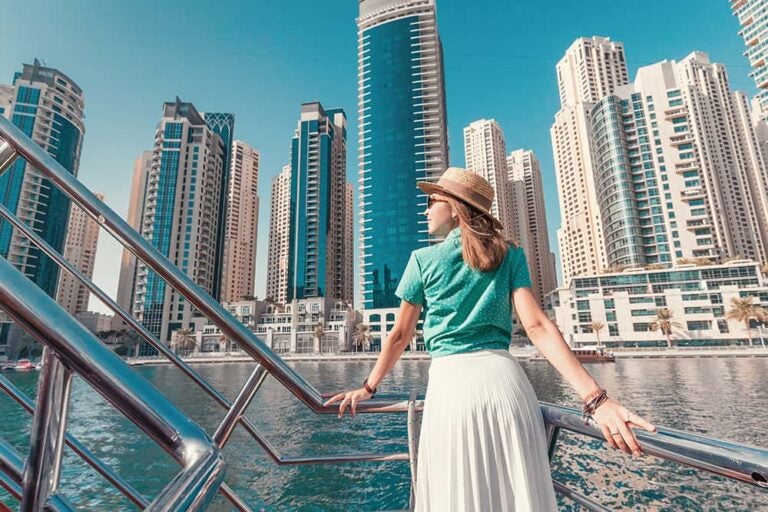 ドバイ旅行の定番スポットであるマリーナ地区の近代的な高層ビル群を、船上から眺める女性の様子