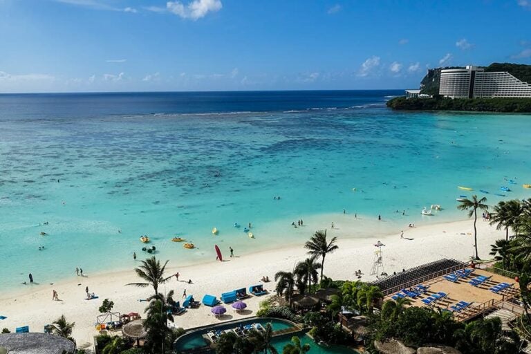 澄み渡る青空とエメラルドグリーンの海が広がるグアムのタモン湾と白い砂浜の全景