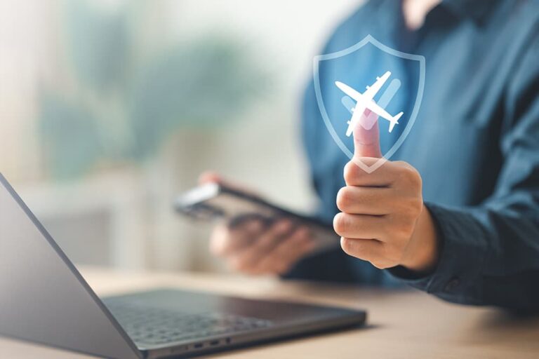 ノートパソコンとスマートフォンを操作しながら親指を立てる人物に、飛行機と盾のアイコンが浮かび上がる、海外旅行のキャンセル保険による補償の安心感を表すイメージ