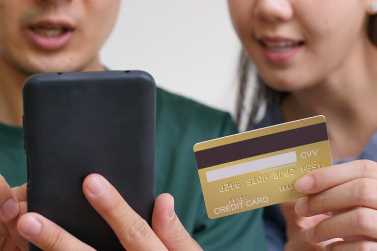 スマートフォンとクレジットカードを手に持ち、海外旅行保険やキャンセル保険のオンライン加入手続きについて相談している男女の様子