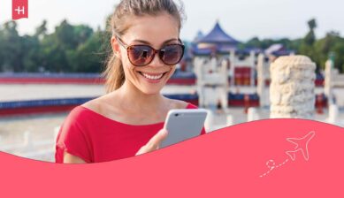 Интернет в Китае для туристов: улыбающаяся туристка со смартфоном на фоне традиционных китайских достопримечательностей.
