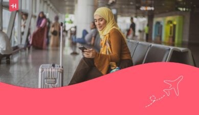 امرأة مسلمة مسافرة تنظر إلى هاتفها في صالة المغادرة، وقد تم اختيار هذه الصورة كصورة رئيسية لمقال يشرح ماهية شريحة eSIM.