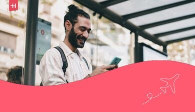 الصحفي المستقل يقرأ هاتفه الذكي بابتسامة، وهو يقف تحت أشعة الشمس تحت سقف محطة الحافلات.