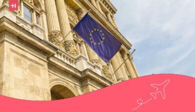 علم الاتحاد الأوروبي يرفرف أمام مبنى كلاسيكي عريق مع أيقونة طائرة بيضاء، كصورة بارزة لمقال عن خدمات التجوال الدولي في أوروبا.