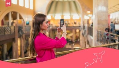 امرأة تلتقط صورة بهاتفها داخل مركز تسوق أثناء استخدام خدمات التجوال الدولي من زين