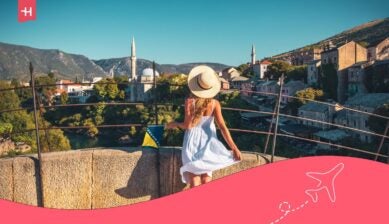 سائحة في موستار، البوسنة، خلفها الجسر القديم والمسجد، رمز لأفضل شريحة بيانات في البوسنة للمسافرين