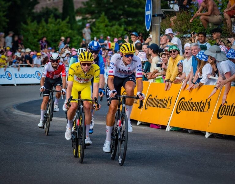 Profesjonelle syklister i Tour de France som runder en sving foran jublende tilskuere.