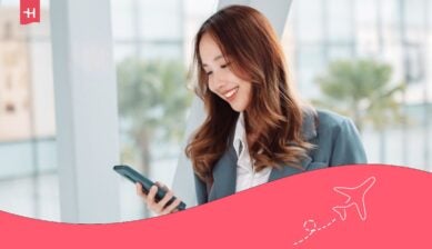 En smilende kvinne som bruker sin Ubigi eSIM på en smarttelefon mens hun er på reise i et lyst og moderne lokale.